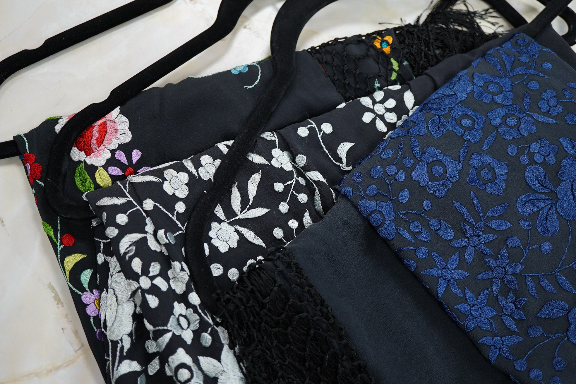 Three Chinese shawls, 1930’s machine floral embroidered, on black silk crepe de chine. One multicoloured, one navy blue, the other white embroidery. Largest navy and white shawls:130cm x 120cm. Condition - no stains, fad